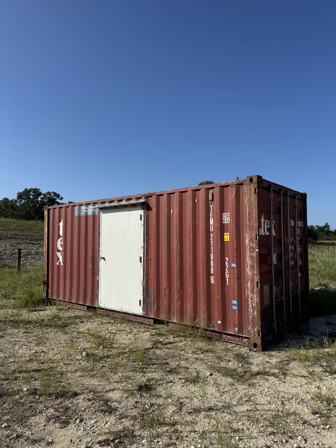 Red shipping container with a white personnel door installed on its side