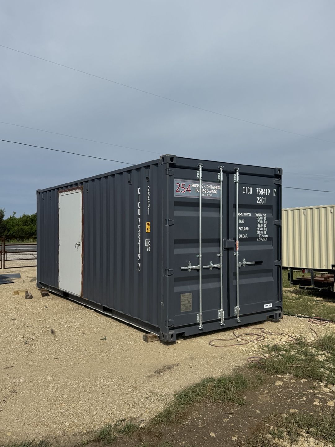 Dark gray container with a white steel personnel door installed on its side