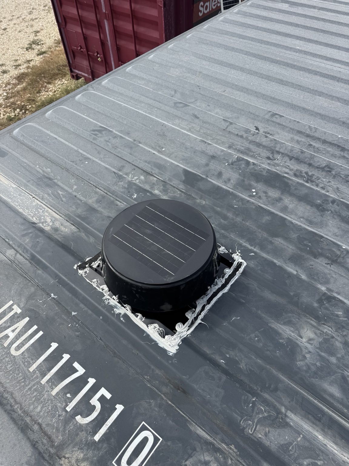 Round black solar-powered roof vent installed on a shipping container