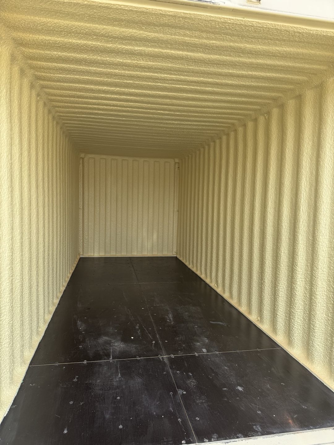 Interior of a shipping container with light-colored spray foam on its walls and ceiling