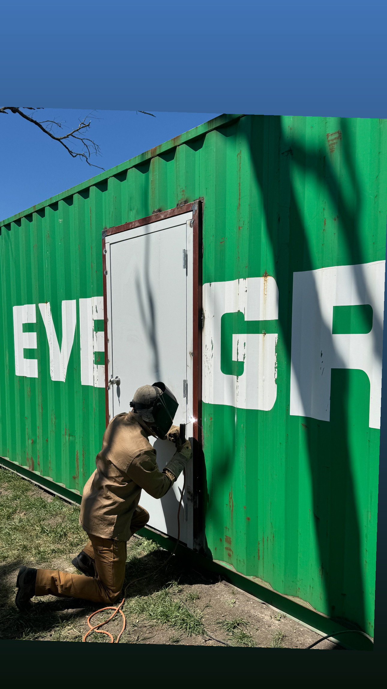 Worker fitting a steel personnel door into a green shipping container